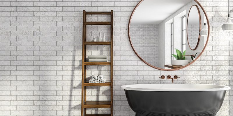 foto de um banheiro reformado no estilo industrial. parede branca de tijolo aparente, uma escada sendo usada como estante ao lado de uma banheira preta e um espelho com moldura de madeira